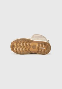 Beige lábbeli, textúrált gumitalppal, amelynek zigzag mintázata van, és egy puha, bordázott felső anyaggal, amely szoros illeszkedést biztosít.