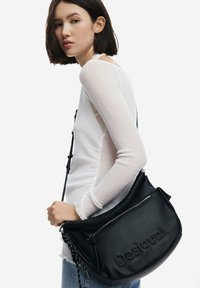 Borsa a mano in pelle nera con logo "Desigual" in rilievo, dotata di una tracolla intrecciata e testurizzata e di una tasca con zip per riporre oggetti.