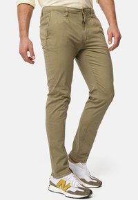Chino en coton vert olive avec une coupe slim, doté d'une fermeture à bouton et à zip, de poches latérales et de détails de couture discrets.