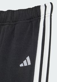Black athletic pants featuring a white striped design, elastic waistband, and a gray logo on the side. Soft, textured fabric.