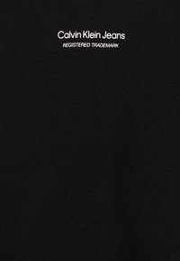 T-shirt in cotone nero con scollo rotondo, con testo bianco "Calvin Klein Jeans" e "REGISTERED TRADEMARK" sottostante in un carattere semplice.