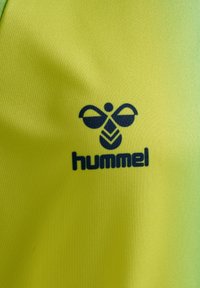 Logo czarnej pszczoły Hummel i nazwa marki na jasnym, żółtym tle tkaniny.