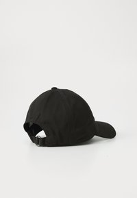 Casquette de baseball noire réglable couchée sur le côté, montrant la sangle arrière avec boucle en métal sur un fond blanc.