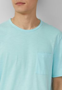 Lichtblauw T-shirt met korte mouwen, gemaakt van zachte stof, met een ronde halslijn en een klein borstzakje aan de linkerkant. Glad textuur, casual ontwerp.