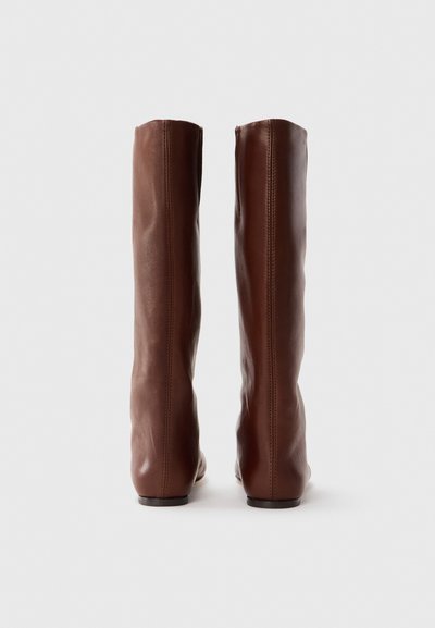 Bottes en cuir marron hautes jusqu'au genou avec une texture lisse, un dessus légèrement effilé et un design minimaliste. Pas de quincaillerie ou d'accents visibles.