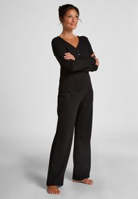 Zwart loungewear set bestaande uit een lang mouwtop met een V-hals en knoopdetail, gecombineerd met wijde broeken, gemaakt van zachte stof.