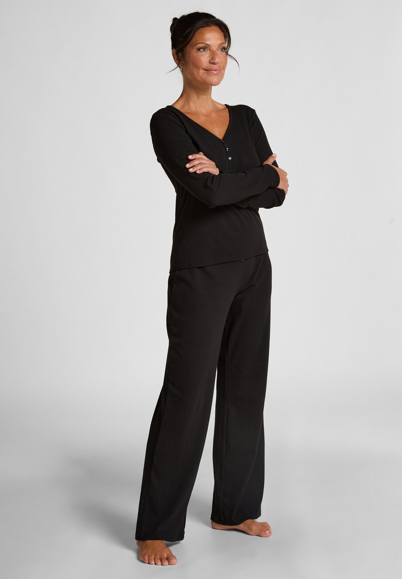 Zwart loungewear set bestaande uit een lang mouwtop met een V-hals en knoopdetail, gecombineerd met wijde broeken, gemaakt van zachte stof.
