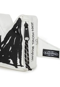 Witte canvas tas met gedurfde zwarte grafische ontwerpen, een ritssluiting en een strap. Merken zijn "Jean-Michel Basquiat" en "EASTPAK."