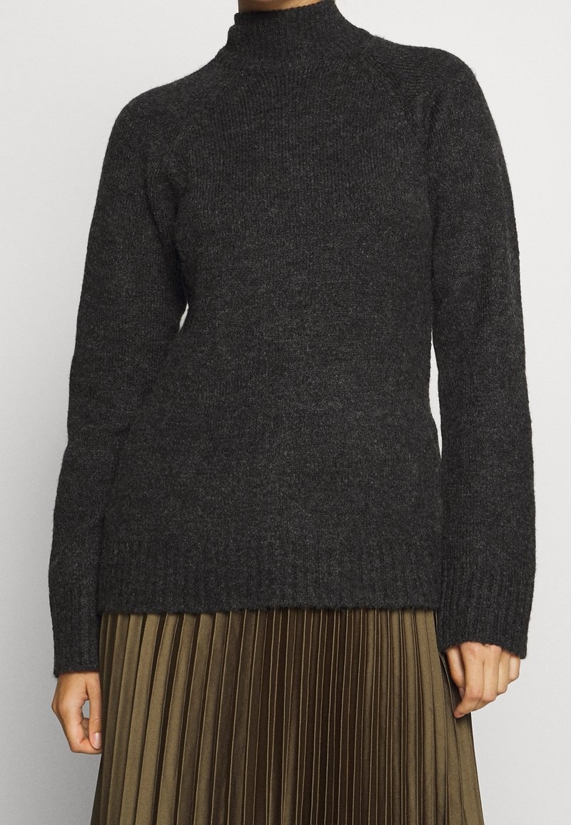 Pull en tricot côtelé gris foncé à manches longues associé à une jupe plissée vert olive, présenté de l'épaule jusqu'à mi-cuisse.