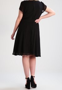 Černé šaty s krátkými rukávy, rozšířenou siluetou a páskem v pase. Zapínání na zip na zádech a průhledná látka na rukávech.