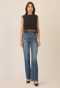 Schwarzes Spitzen-Crop-Top mit gewellten Kanten, kombiniert mit hellblauen Schlagjeans. Die Jeans haben ein klassisches Fünf-Taschen-Design und eine dezente Ausbleichung.