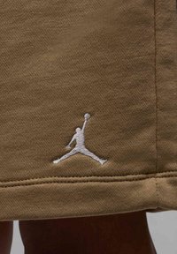 Pantaloni corti in tessuto marrone con logo Jumpman ricamato di colore bianco sul lato sinistro in basso. La texture è liscia e presenta un motivo di trama uniforme.