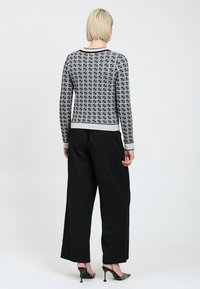 Maglione a maglia con motivo in bianco e nero, maniche lunghe, scollo rotondo, orlo a coste, abbinato a pantaloni neri larghi e tacchi.