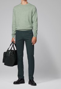 Jasnozielony sweter z teksturą, ciemnozielone spodnie zwężane, czarne skórzane buty oraz czarna torba z szarymi uchwytami i zamkiem błyskawicznym.