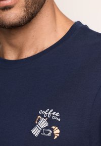 Navy blue cotton t-shirt with a round neck and short sleeves, featuring embroidered "coffee time" design with a coffee pot, cup, and croissant.