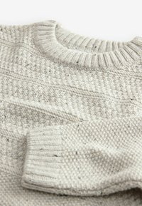 Pull en maille gris clair avec un motif texturé, col rond côtelé et poignets côtelés. Le matériau semble doux et chaud.