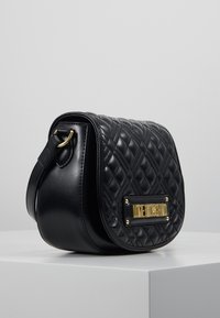 Černá prošívaná crossbody taška z umělé kůže. Disponuje kováním ve zlaté barvě a na přední straně má značkovou destičku. Zaoblený tvar.