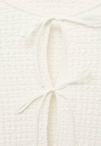Top in tessuto bianco testurizzato con chiusura a nodo al collo, caratterizzato da un sottile motivo a quadri e una superficie morbida.