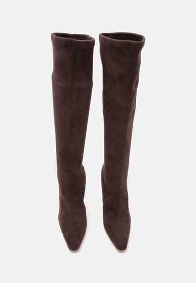 Paire de bottes hautes en daim marron foncé avec des bouts pointus et une tige fine et ajustée s'étendant au-dessus du genou sur fond blanc.
