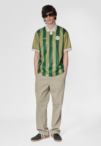Grøn- og guldstribet polo tee med hvid krave, parret med beige bukser og sorte sneakers med hvide striber.