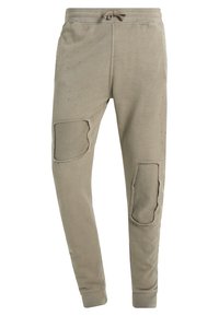 Beige Sweatpants mit einem Kordelzug an der Taille, die über strukturierte Patches an den Knien, gerippte Bündchen und ein weiches, abgenutztes Aussehen verfügen.