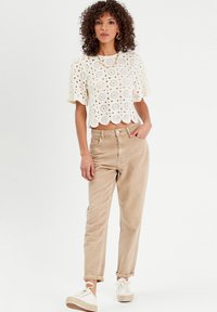 Haut court en crochet blanc avec un motif floral, associé à un pantalon en velours côtelé beige clair et des baskets blanches à plateforme. Design simple et décontracté.