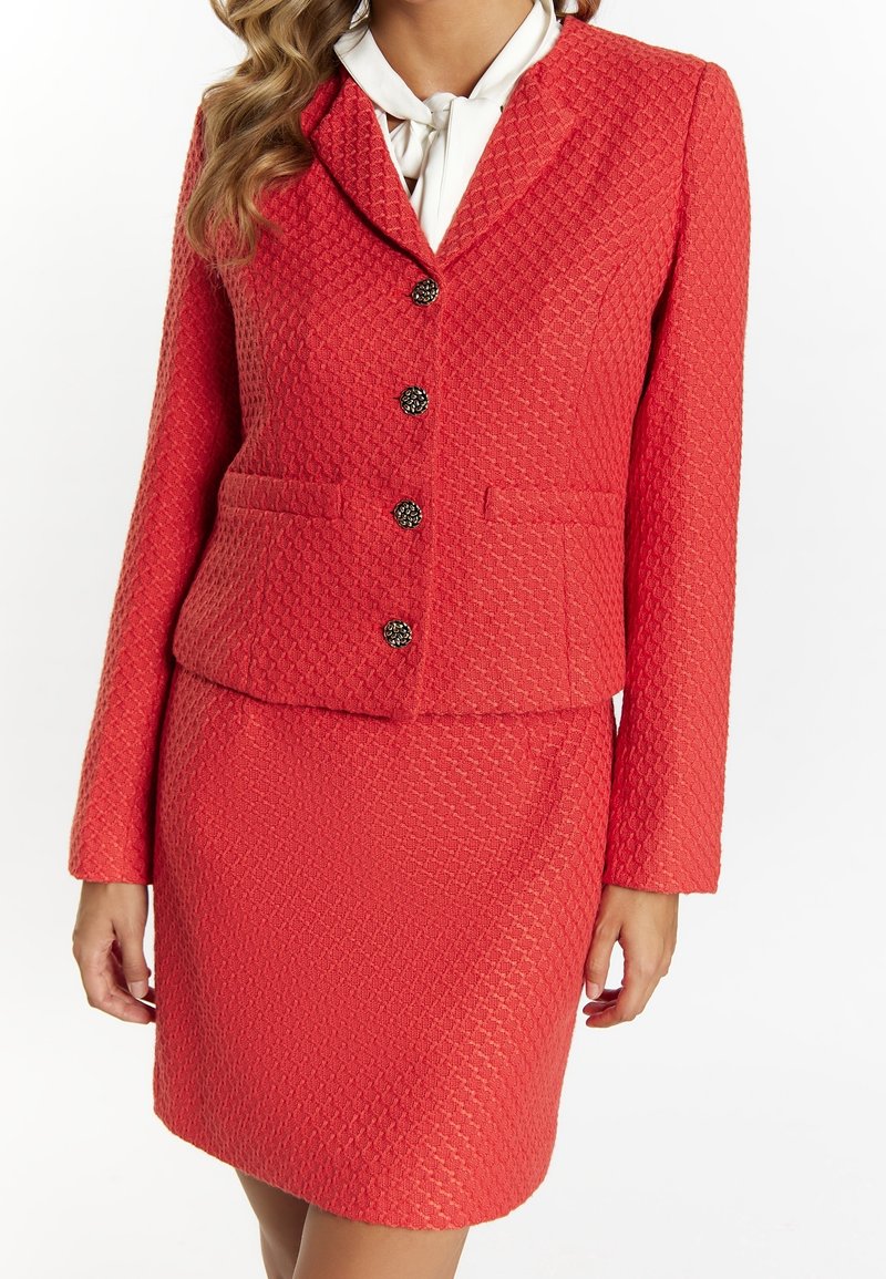 Blazer texturé corail avec jupe ajustée assortie. Comprend deux poches, cinq boutons décoratifs et un col classique.