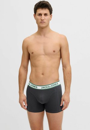 Skjorteløs mann som står, iført mørkegrå bokserbriefs med en hvit midjebånd med grønn "JACK & JONES"-tekst.
