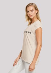 Beige cotton t-shirt with rolled sleeves, featuring a black mountain outline graphic on the front. The design is casual and fitted.