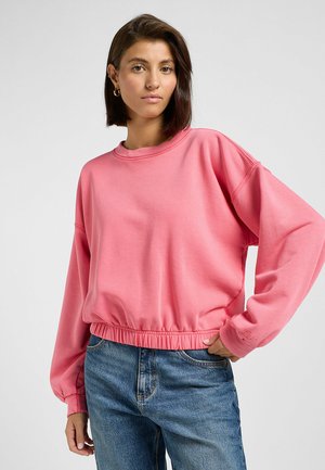 Felpa corta rosa con maniche lunghe, caratterizzata da un orlo a coste e dettaglio del logo ricamato. Abbinata a jeans blu.