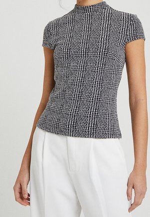 Lyhyet hihattomat mustavalkoinen toppi korkealla kauluksella, valmistettu teksturoidusta kankaasta, jossa on hienovarainen kuvio ja tiukka siluetti.