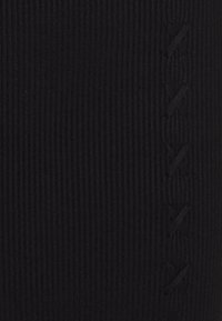 Leggings en tissu noir côtelé présentant un motif texturé et un détail décoratif torsadé sur le côté. Conception extensible et ajustée.