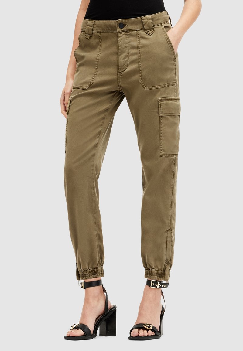 Femme portant un pantalon cargo vert olive avec des poches plaquées à l'avant et des chevilles élastiques, assorti à des sandales à talons hauts noires.