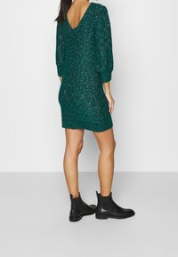 Abito di maglia turchese con scollatura a V sul retro, maniche a sbuffo 3/4 e un finish testurizzato. Abbinato a stivali neri alla caviglia. Semplice, di lunghezza corta.
