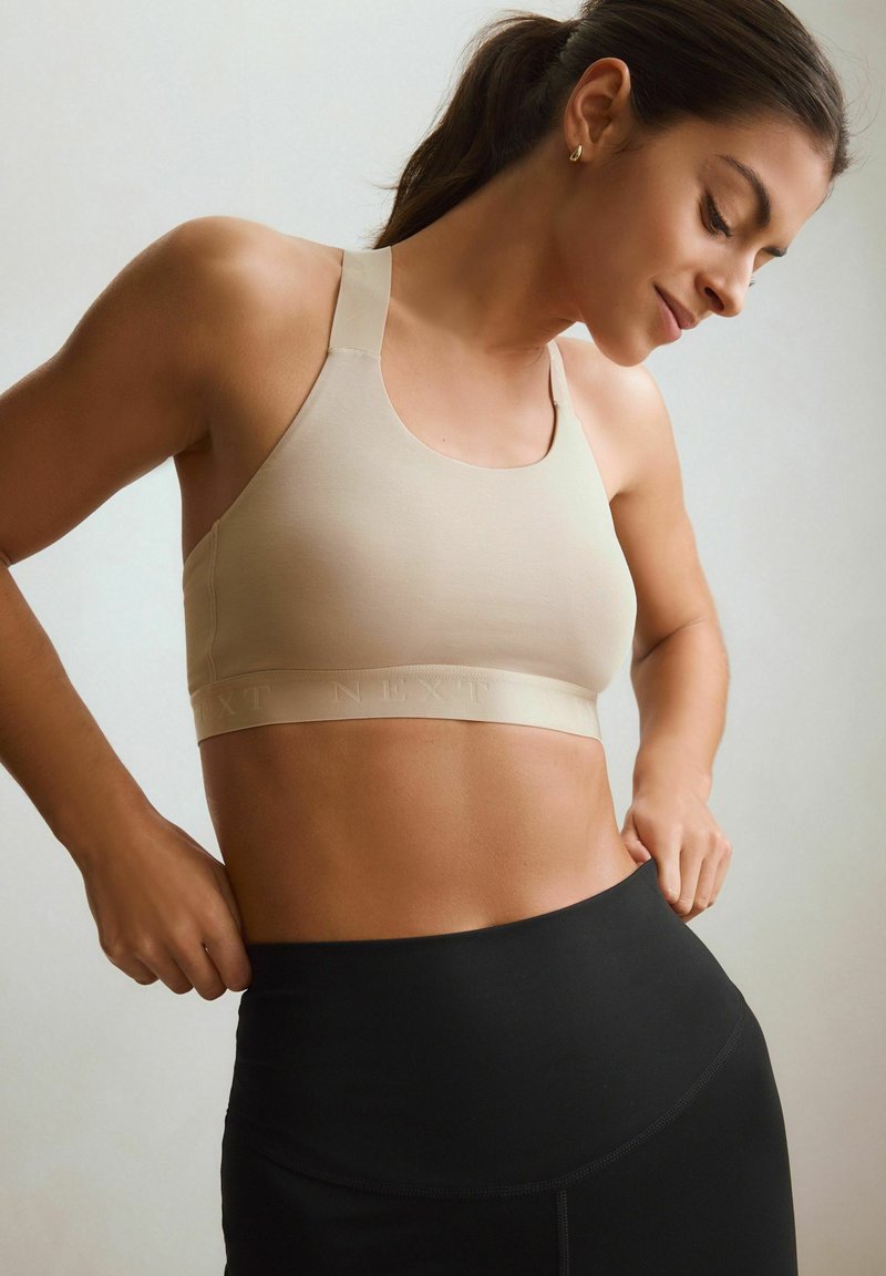 Beige sportbh med breda band och en band prytt med logo. Slät material med en figurnära passform, kombinerad med svarta högmidjade leggings.