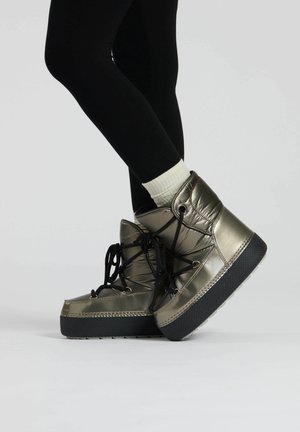 Metallic olive green ankle boots with a padded design, black laces, and textured black rubber soles, worn with black leggings and white socks.