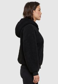 Black fleece hoodie with a spacious hood, ribbed cuffs, and relaxed fit. Soft texture, featuring a solid color without patterns.