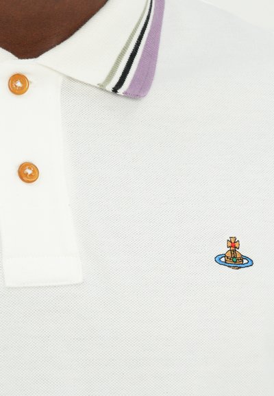 Balts polo krekls ar teksturētu adījumu, ar purpursarkanu un melnu svītru apkakli, trim oranžām pogām un nelielu izšūtu dizainu.