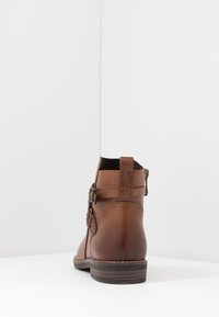 Braune Leder-Stiefelette mit einem seitlichen Schnallen-Detail, texturiertem Rücken und genähten Akzenten an Sohle und Oberteil. Flacher Absatz, lässiges Design.