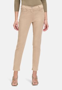 Pantalons beiges ajustés avec une texture lisse, taille mi-haute et poches avant, associés à des talons hauts à lanières de teinte neutre.