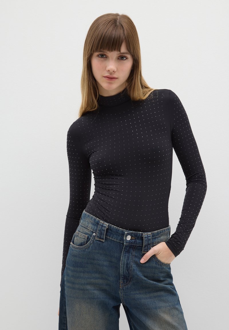 Top nero a maniche lunghe con collo alto, caratterizzato da un motivo a pois. Abbinato a jeans di jeans blu a vita alta leggermente strappati.