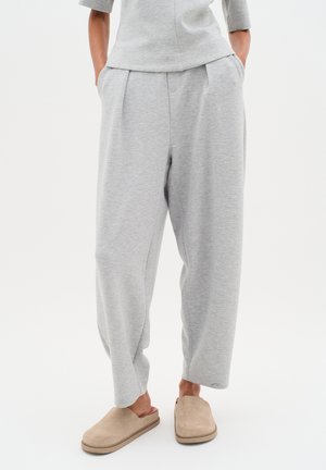 Hellgraue, locker sitzende Sweatpants mit Falten, seitlichen Taschen und schmal zulaufenden Bündchen, aus einem weichen Baumwollmix gefertigt. Kombiniert mit tanfarbenen Slip-On-Schuhen.