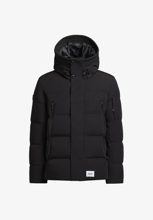 Schwarze Pufferjacke mit hohem Kragen und Kapuze, mit gepolsterten Einsätzen und seitlichen Reißverschlüssen. Getragen mit schwarzen Cargo-Hosen und Stiefeln.