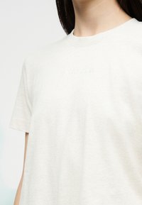 Λευκό κοντομάνικο μπλουζάκι με διακριτικό ανάγλυφο λογότυπο "Calvin Klein", φορεμένο από άτομο με σκοτεινά μαλλιά, σε απλό ανοιχτό φόντο.