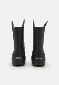 Para czarnych kaloszy Crocs widocznych z tyłu, z teksturowanym obcasem i uchwytami, na białym tle.