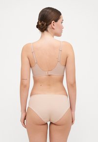Nude undergarments featuring a seamless bralette with adjustable straps and scalloped-edged bottom. Smooth texture and simple design.