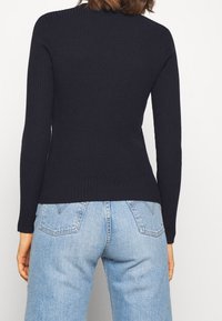 Gebreide ribfluwelen top met lange mouwen in donker marineblauw, getailleerd ontwerp met een ronde halslijn, gecombineerd met lichtblauwe hooggetailleerde jeans.
