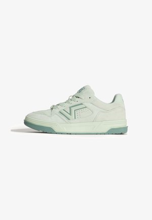 Lichtgroene lage sneaker met vetersluiting, gestructureerde zool en V-vormig logo aan de zijkant, gezien vanaf de buitenkant.