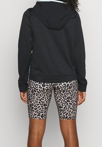 Svart huvtröja med långa ärmar, kombinerad med cykelshorts i leopardmönster. Mjukt material, figurnära design och framträdande mönster.