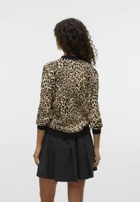 Bunda bomber se vzorem leopardí srsti, s černým límcem a náplety, vyrobená z hladké tkaniny, v kombinaci se šedou skládací sukní.
